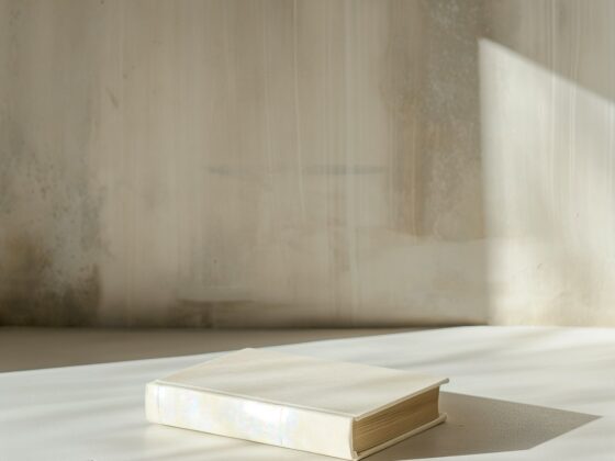Livre fermé à couverture crème posé sur une surface blanche, éclairé par une lumière douce dans un décor minimaliste.